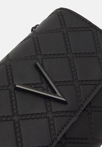 Černá kožená taška s prošitým vzorem čtvercových tvarů a řetízkovým zdobením. Zdobená trojúhelníkovým černým kováním.