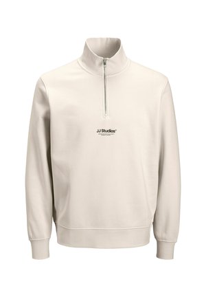 Helle beige Kapuzenjacke mit hochschließendem Kragen und einem Viertelreißverschluss. "JJ Studios"-Logo auf der Vorderseite gedruckt, weicher Stoff und gerippte Bündchen.