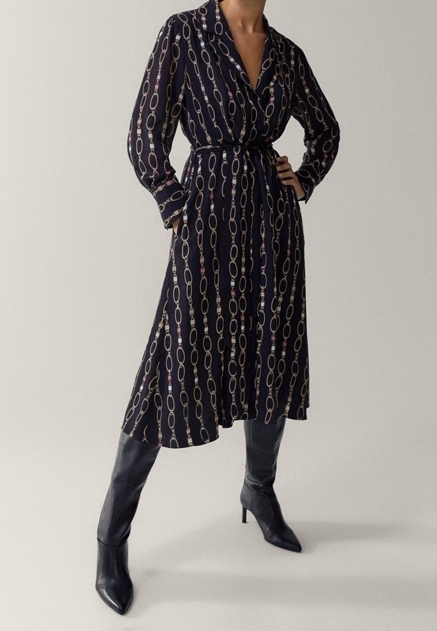 Pitkähihainen tummansininen mekko, jossa on valkoisia ja vaaleanpunaisia ketjumaisia kuvioita, vyötärövyö ja kaulus. Yhdistetty polven ylle ulottuviin mustiin korkokenkiin.