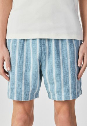 Blaue und weiße, vertikal gestreifte, strukturierte Shorts, getragen mit einem schlichten weißen Oberteil, die bis zur Mitte des Oberschenkels reichen und Seitentaschen haben.