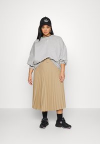 Felpa grigia oversize, gonna beige plissettata, sneakers nere, cappellino nero con logo, collane sovrapposte, vestibilità rilassata, texture morbida.