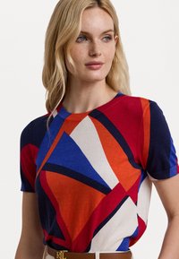 Short-sleeve knit top featuring a multicolored geometric pattern in red, blue, cream, and navy with a ribbed crew neckline.