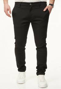 Schwarze Slim-Fit-Hosen mit glatter Oberfläche, mit Knopfverschluss, Seitentaschen und elastischen Bündchen, kombiniert mit weißen Sneakers.