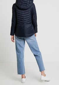 Chaqueta de navidad acolchada con capucha y patrón de rombos, combinada con vaqueros de pierna ancha azul claro y zapatillas blancas.