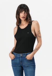 Débardeur noir à larges bretelles et à encolure ronde, fabriqué dans un tissu lisse. Associé à un jean bleu avec poches avant.