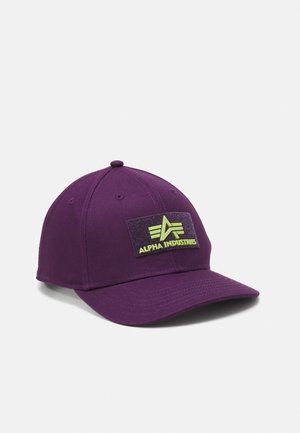 Purple cap with a flat visor, featuring a green Alpha Industries patch on the front. Made of fabric with stitched details and eyelets.
