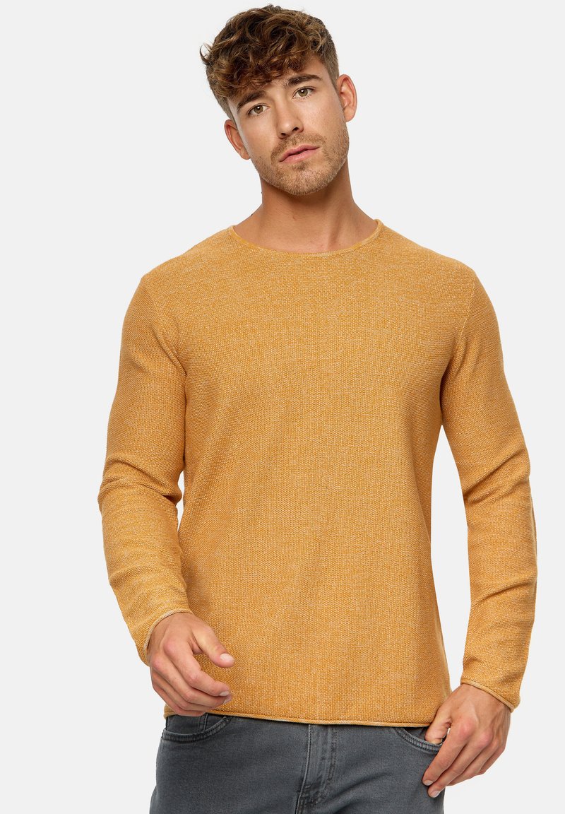 Senfgelbes, strukturiertes Langarmshirt mit Rundhalsausschnitt und eng anliegenden Ärmeln, kombiniert mit grauen Jeans.