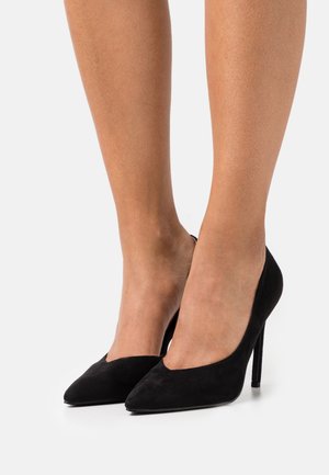 Escarpins noirs en daim à talons hauts avec bouts pointus et encolure en V peu profonde. Des talons fins en stiletto ajoutent de la hauteur et de l'élégance.