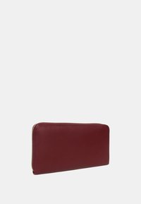 Portafoglio in pelle rossa con forma rettangolare, caratterizzato da una superficie liscia e una zip dorata lungo un lato. Design minimalista, senza motivi visibili.