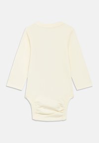 Langärmiger Baby-Body aus cremefarbenem Baumwollstoff, mit Rundhalsausschnitt, weicher Textur und gerafften Details am Saum.
