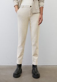 Pantalons beige à motif chevrons avec poches latérales et coupe slim, associés à des bottines à talons épais noires.