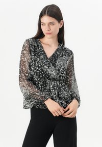 Blusa nera a fiori con maniche lunghe trasparenti, scollatura a V, vita arricciata, caratterizzata da piccoli motivi floreali bianchi e grigi su uno sfondo scuro.