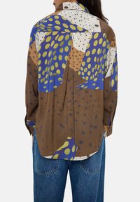 Koszula w wzory w kolorze brązowym, niebieskim i zielonym z dużymi kropkami. Posiada kołnierzyk, długie rękawy i luźny krój. Gładka tekstura materiału.