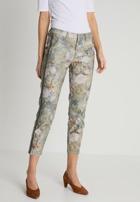 Pantalons à imprimé floral en vert et beige, avec une coupe slim, des poches en biais et un tissu légèrement texturé. Assortis à des chaussures à talons marron.