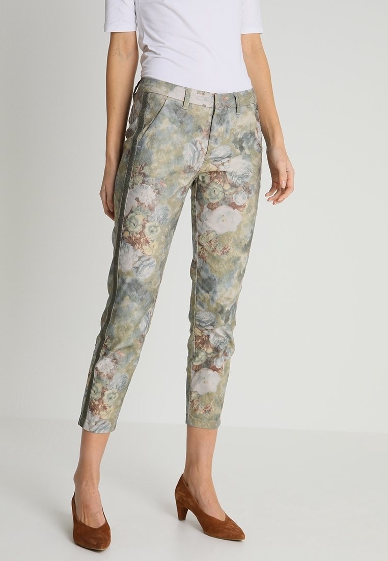 Pantalons à imprimé floral en vert et beige, avec une coupe slim, des poches en biais et un tissu légèrement texturé. Assortis à des chaussures à talons marron.