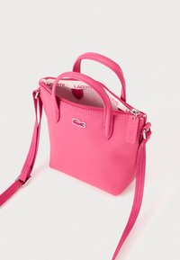 Sac à main rose en matériau texturé, doté de deux poignées supérieures, d'une bandoulière amovible et d'une fermeture zippée avec un accent de logo.
