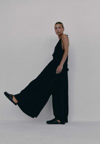 Czarny kombinezon bez rękawów z szerokimi nogawkami, wykonany z lekkiego materiału. Zestawiony z czarnymi butami wsuwanymi z metalowymi elementami.