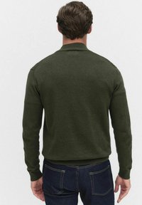 Tummanvihreä neulepusero, jossa on pitkät hihat ja ribbireuna, yksinkertaisella designilla ilman kuvioita tai koristeita, katsottuna takaa.