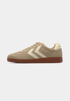 Beige ruskinds sneakers med lysecreme detaljer og en brun gummisål. Har snørebånd og et zigzag mønster på siderne.