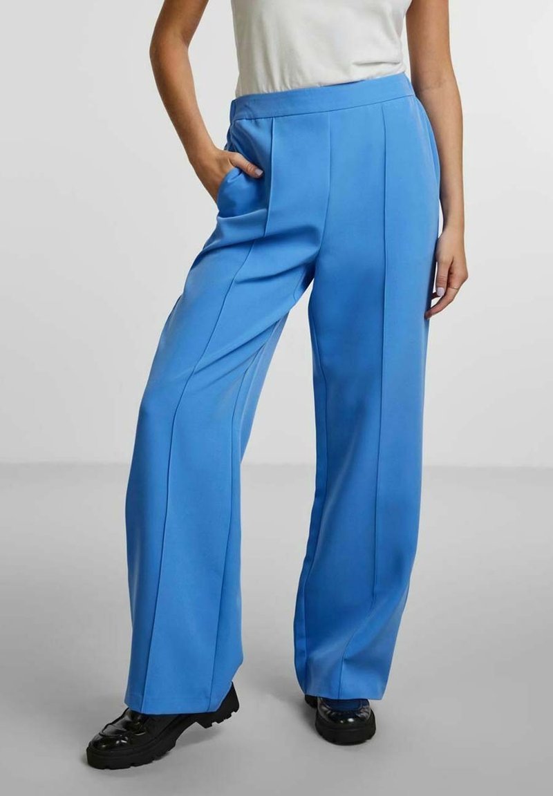 Vidbralla i klarblått tyg, med frontveck och sidofickor. Aningen kragen med en enkel topp och svarta klumpiga skor.