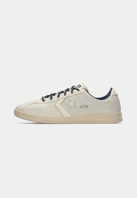 Lys grå semskede sneakers med en marineblå krage, med en hvit stjerne logo og mørkere lisser, kombinert med en kremfarget gummisåle.