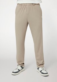 Šviesiai smėliniai džinsai su lanksčiu liemeniu, lygiu paviršiumi, šoninėmis kišenėmis ir mažu logotipo akcentu kairėje šlaunyje.