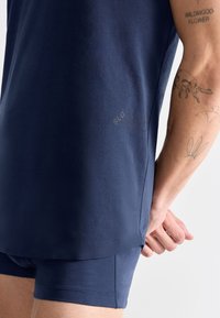 T-shirt in cotone blu navy con orlo arrotondato, abbinato a pantaloni corti abbinati; presenta un logo discreto sul lato e una texture liscia.