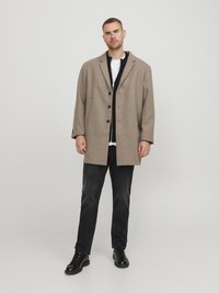 Abrigo de mezcla de lana beige con solapas de muesca, tres botones frontales y un corte relajado, combinado con jeans de mezclilla negros y botas negras.