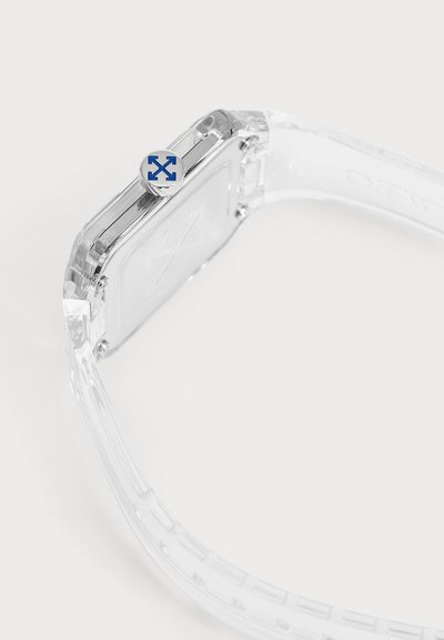 Bracelet de montre transparent avec un boîtier carré clair et une couronne argentée avec des flèches bleues sur fond blanc.