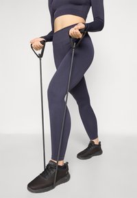 Navy ribbed leggings and long-sleeve top paired with black mesh athletic shoes, holding black resistance bands.