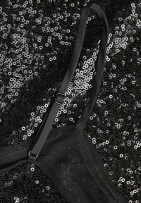 Sort sequin-stof med et mesh-design, prydet med glitrende, runde pailletter og en justerbar sort rem med metal-slider detalje.