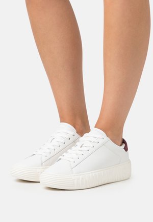Białe skórzane sneakersy z teksturowaną gumową podeszwą, z bordowym akcentem na pięcie i wytłoczonym logo "TOMMYJEANS" po boku.