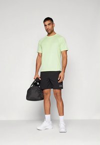 Camiseta deportiva de manga corta verde claro con pantalones cortos negros, zapatillas blancas y una bolsa de gimnasio negra. Tela suave con un ajuste relajado.