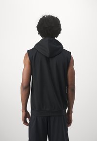 Fekete ujjatlan kapucnis pulóver vastag kapucnival, puha tapintással és laza szabással; a hozzáillő fekete sorttal kiegészítve, hátulról nézve.