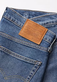 Jeans en denim bleu moyen avec un patch en cuir texturé. Dotés de coutures orange, d'une braguette à boutons et d'un design à cinq poches. Taille W32 L32.