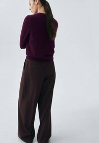 Burgunderfarbener Wollpullover kombiniert mit hoch taillierten, weiten braunen Hosen. Texturiert, lässige Passform mit geripptem Saum und Rückennähten.
