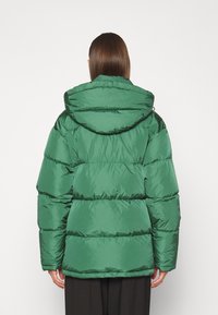 Veste matelassée verte avec capuche, présentant un design matelassé, une texture brillante et des manches larges pour l'isolation et le confort.