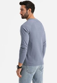 Pitkähihainen, ribattu t-paita vaaleansinisessä, jossa on pyöreä kaula-aukko ja kapea siluetti, yhdistettynä vaaleisiin farkkuihin.