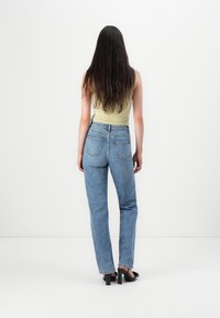 Lichtgroene mouwloze top, blauwe rechte jeans met een hoge taille en zwarte open teen hakken. Zichtbare achterzakken en naaidetails op de jeans.