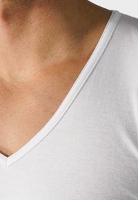 White, cotton t-shirt with a V-neck design, featuring a smooth texture and fine ribbing along the neckline.