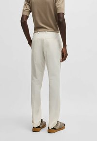 Pantaloni bianchi testurizzati con vestibilità dritta e tasche posteriori, abbinati a calzature beige. L'outfit presenta un top a maniche corte in tonalità neutra.