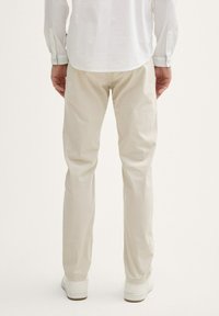 Lichtbeige broek van een zachte stof, met een rechte snit en subtiele textuur. Gecombineerd met witte sneakers.