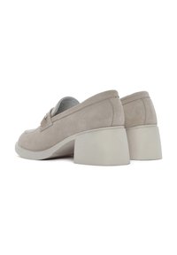Mocassini con tacco in suede beige, dalla punta arrotondata e tacco spesso, caratterizzati da una texture liscia e un design minimalista.