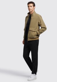 Khaki jack met hoge kraag, twee voorzakken en een ritssluiting. Gekocht met zwarte broeken en witte sneakers. Glad materiaal, modern ontwerp.
