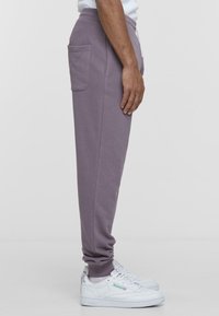 Lilla joggebukser med en avslappet passform, sidelommer og ribbede mansjetter, kombinert med hvite sneakers med grønne detaljer.