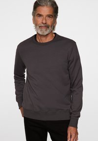 Mörkgrå sweatshirt med långa ärmar, rundad halsringning, ribbade ärmslut och fåll, med en subtil logotyp på bröstet, tillverkad av mjukt tyg.