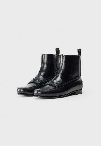 Svarta läderankelstövlar med en slät yta, dragkedjestängning, kontrasterande remmar och en platt klack. Framsöm i loafermodell.