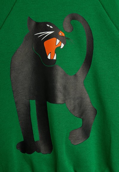 Μαύρη πάνθηρας με ανοιχτό στόμα και αιχμηρά δόντια, γραφικό σε πράσινο υφασμάτινο φόντο, με ουρά καμπυλωμένη προς τα πάνω.