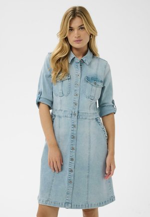 Hele sinise teksariidest särkkleit, millel on lühikesed üleskeeratud varrukad, nööpkinnitused, kaks rinnataskut ja õmbluse detailid. Laienev siluett kuni põlveni.