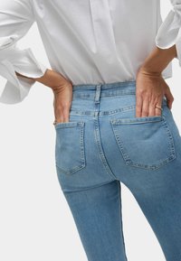 Jeans de tiro alto en azul claro con piernas rectas, que cuentan con un diseño de cinco bolsillos y un desgaste sutil. Tela de denim texturizada.
